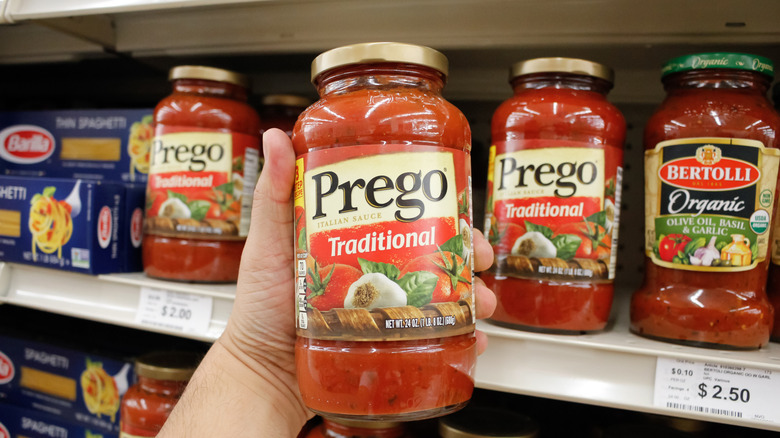 A customer holding a jar of Prego Traditional pasta sauce with other sauces and pastas in the background.