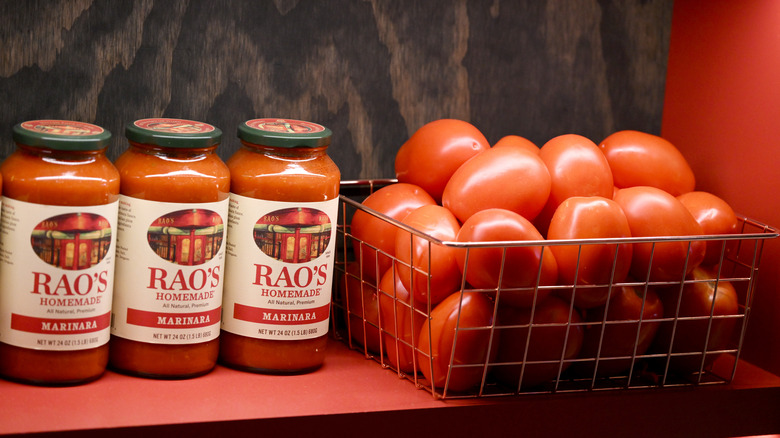 Three jars of Rao's homemade marinara sauce next to a basket of fresh Roma tomatoes.