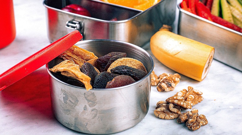 Open stainless steel snack containers filled with fresh and dried fruit and nuts
