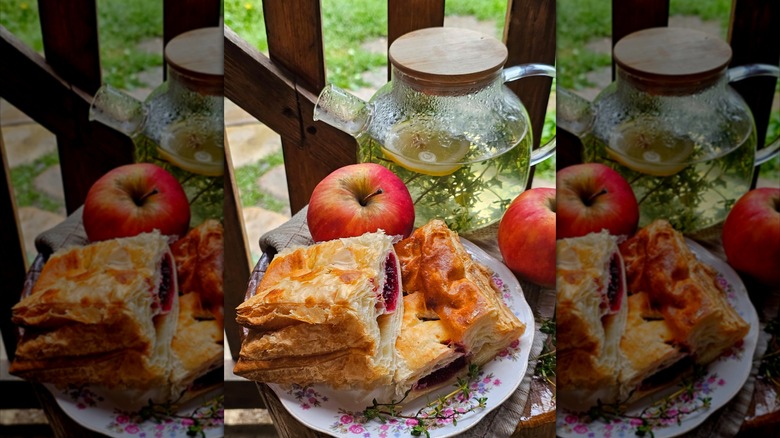 Apple pie puff pastry on a floral plate next to an apple and lemon water