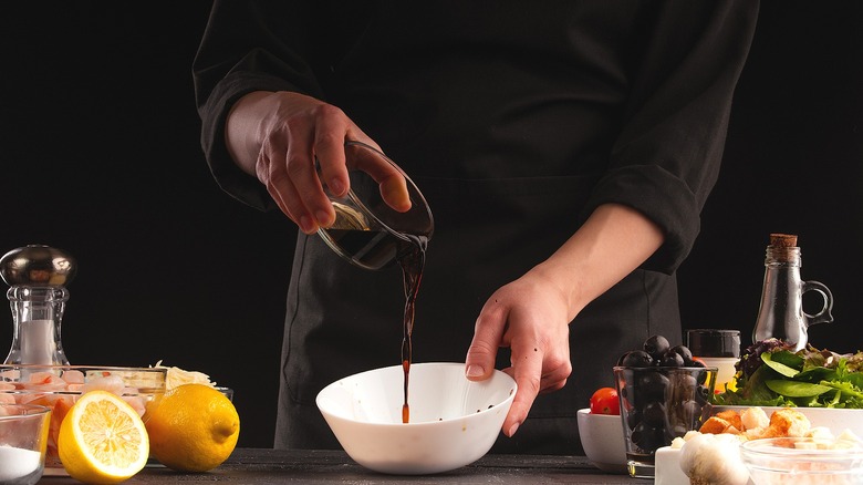 Hands pouring balsamic vinegar into a white bowl