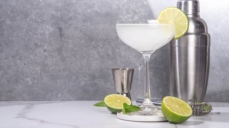 a gimlet in a coupe glass with a few bartending tools behind it