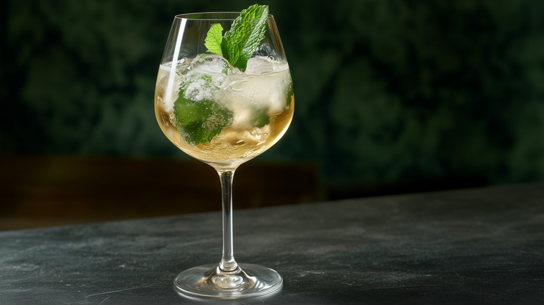 a Hugo spritz topped with sprig mint on a dark green background