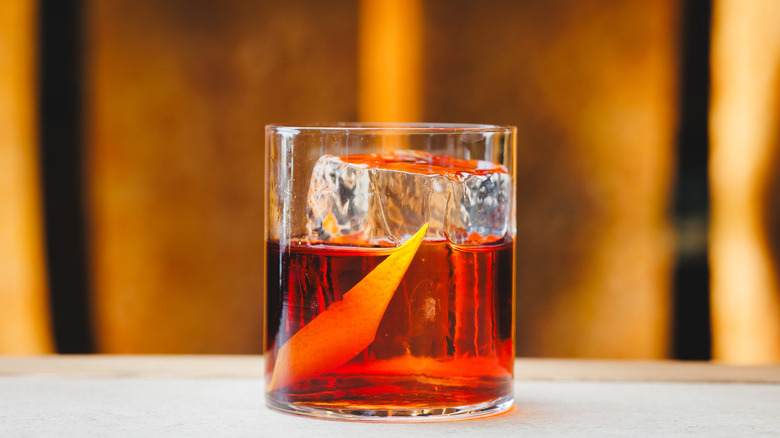a Negroni with orange peel and a big rock ice cube in a modern glass