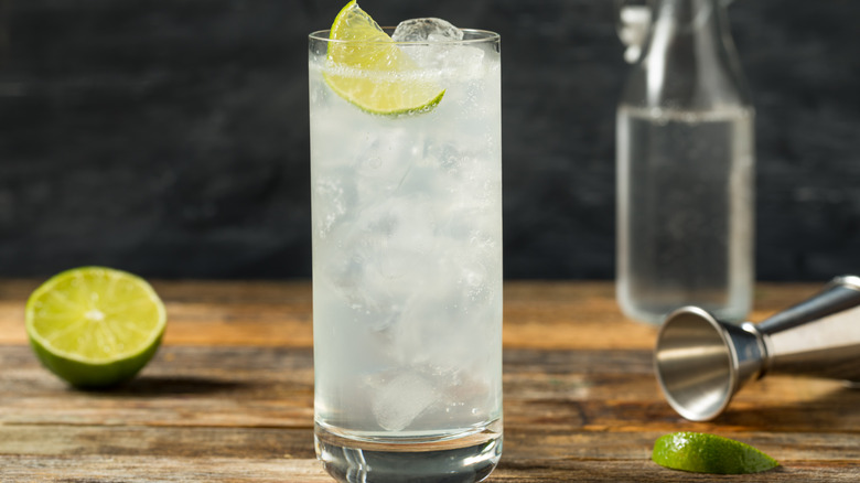 a glass of ranch water in a collins glass with sliced lime and jigger in the background