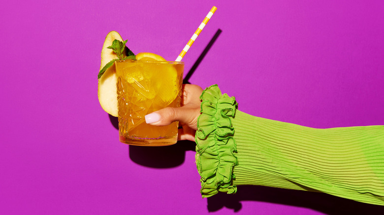 a lady wearing a green dress holding a screwdriver behind a pink background