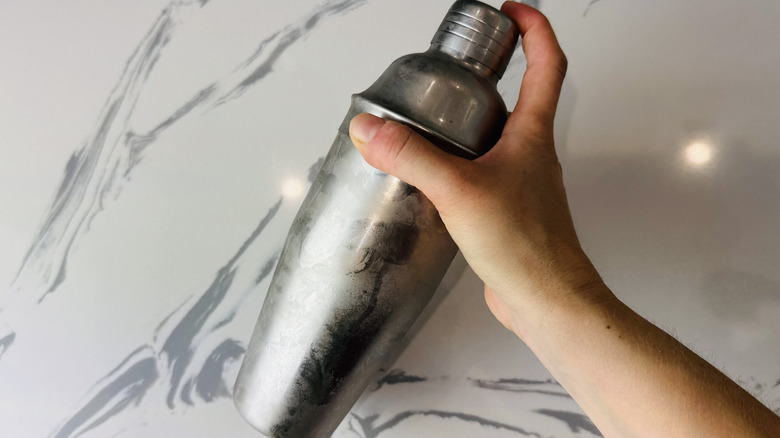 hand holding a cocktail shaker over marble surface