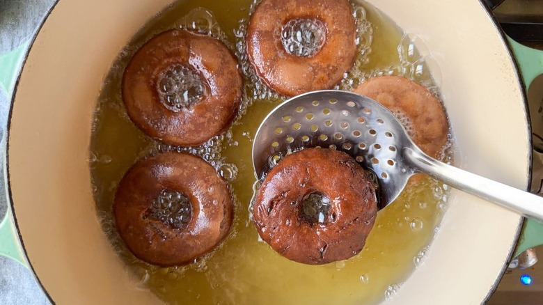 Removing Nutella donut from frying oil in pot with slotted spoon
