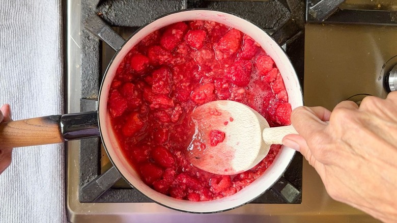 Stirring fresh raspberries in saucepan on stovetop with wooden spoon