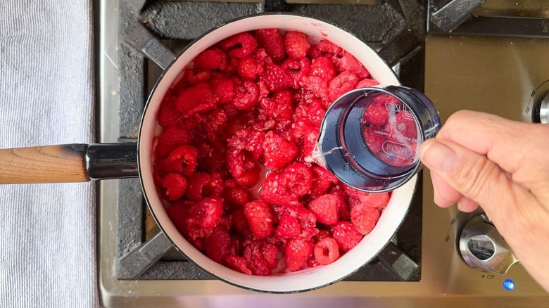 Pouring water into saucepan with fresh raspberries