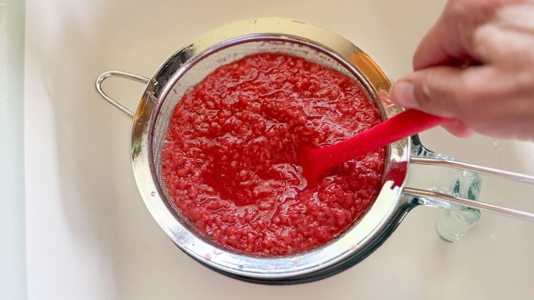Pushing fresh raspberry puree through mesh strainer with spatula