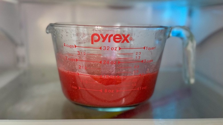 Raspberry puree in glass measuring container in refrigerator
