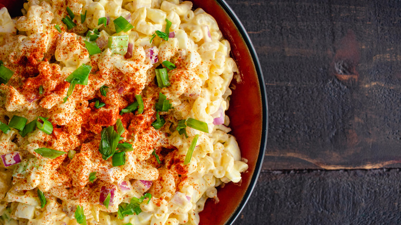 An overhead shot of a bowl of macaroni salad topped with scallions and cayenne pepper
