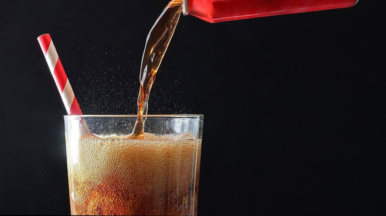 A red can of fizzy cola being poured into a glass with a red and white straw.