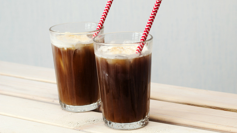 Tall glass mug with fizzy brown soda and foamy cream.