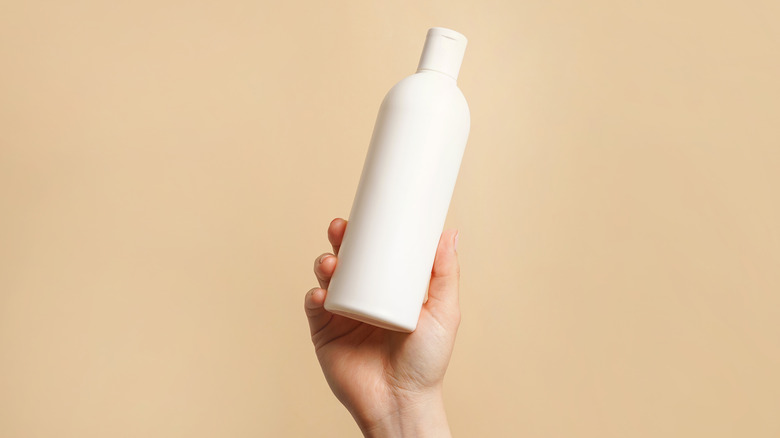 A hand holding a bottle of shampoo