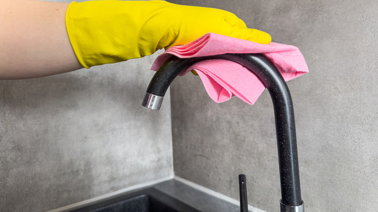 Someone cleaning a kitchen faucet with a sponge