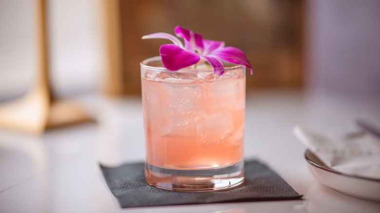 Guava cocktail or mocktail in a rocks glass garnished with a pink orchid