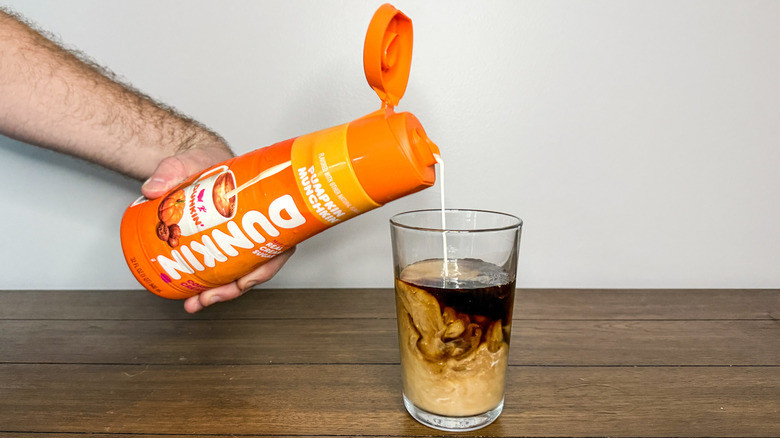 Hand pouring Dunkin' pumpkin coffee creamer