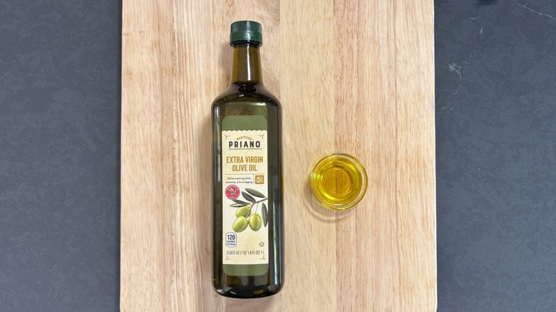 Priano extra virgin olive oil bottle next to glass dish on wooden cutting board and black counter