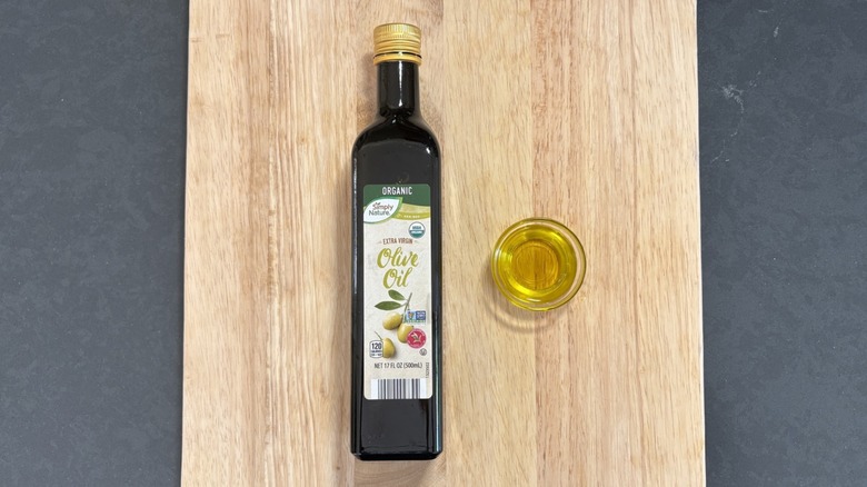 Simply Nature extra virgin olive oil bottle next to glass dish on wooden cutting board and black counter