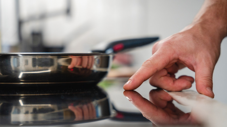 A hand pressing a sensor on an induction cooktop with a pan sitting on the burner