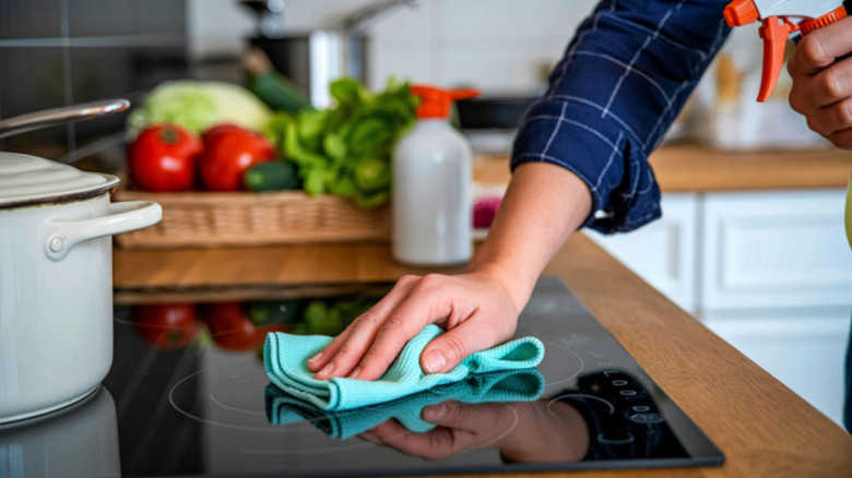 A person using a cleaning cloth to clean an induction cooktop
