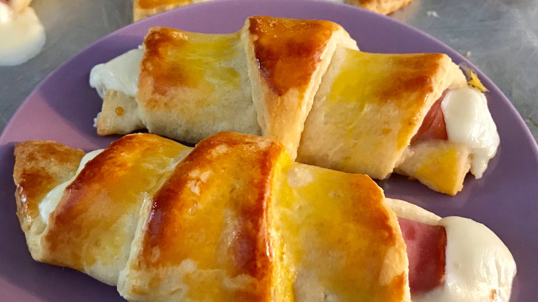 Cooked ham and cheese wrapped in crescent rolls on purple plate.