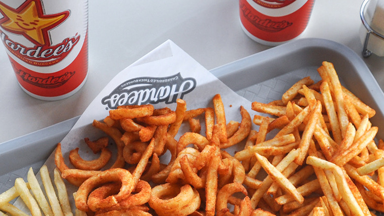 A grey tray filled Hardee's french fries, including their curly fries, alongside two drinks
