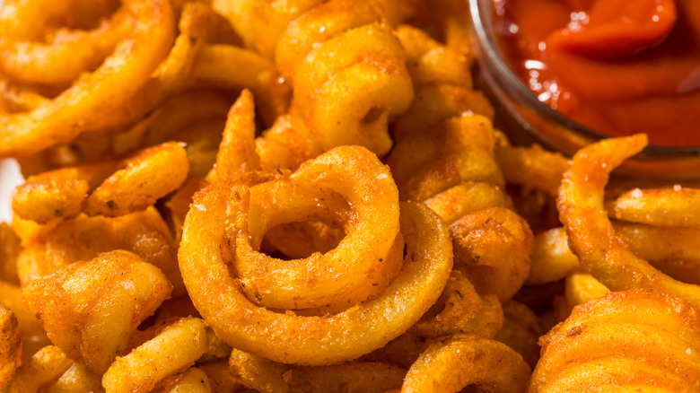 A pile of seasoned curly fries with a small bowl of ketchup