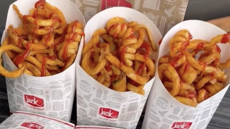 Three containers of Jack in the Box curly fries drizzled with ketchup