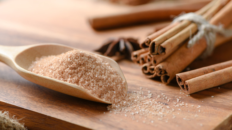 A big scoop of cinnmon sugar is photographed near bundles of cinnamon sticks.