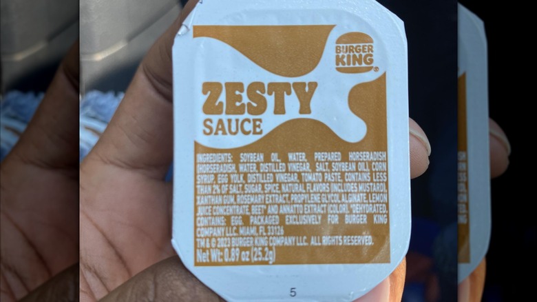 Person holding a container of zesty sauce