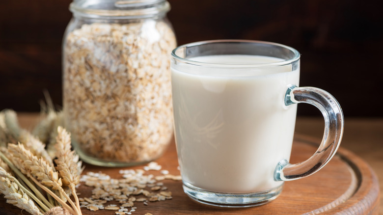 Cup of milk on a wooden surface in front of a glass mason jar of oats.