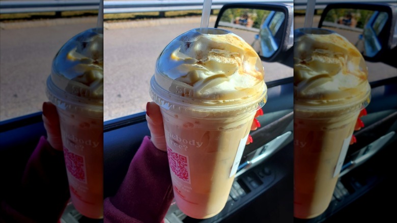 Woman's hand with red nails holding up an iced Dunkin' Pumpkin Spice Signature latte inside a car.