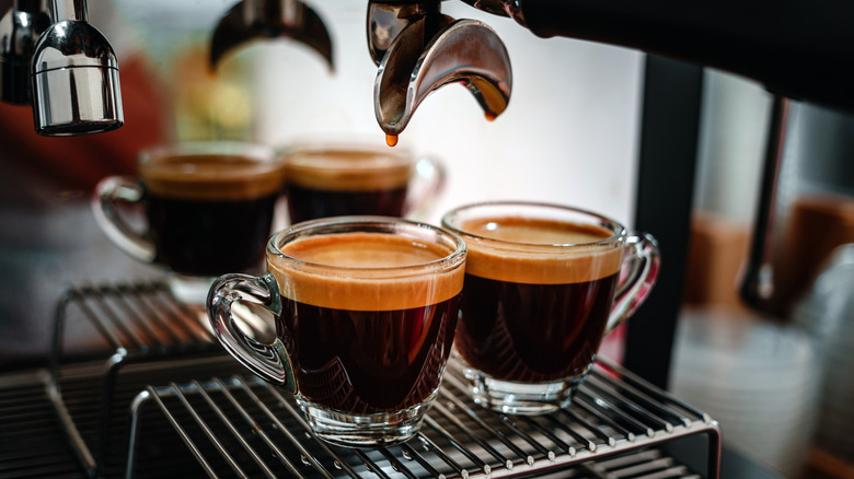 Espresso shots in glass cups under espresso machine spout with espresso still dripping into cups.