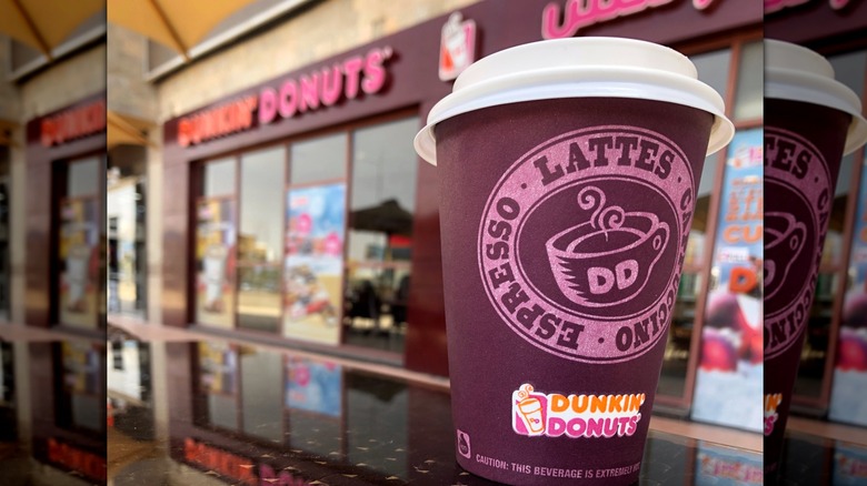 Dunkin' latte in a purple cup on a counter outside of a Dunkin' storefront.