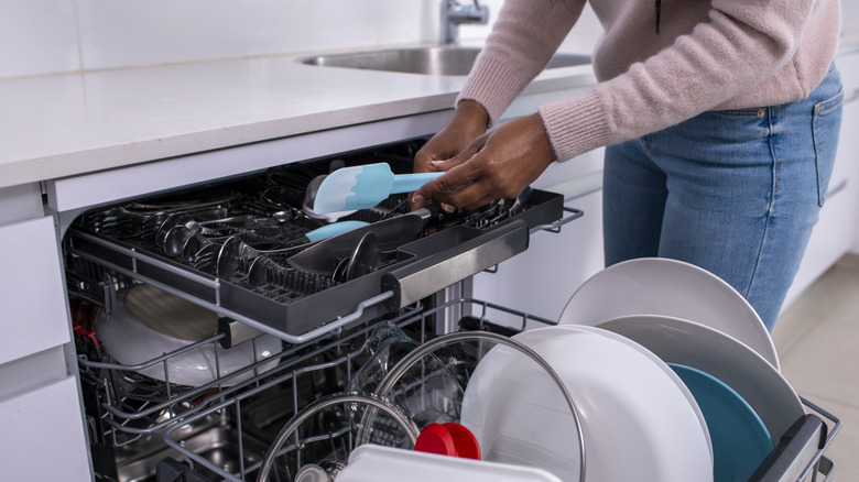 Woman loading utensils into third rack of dishwasher