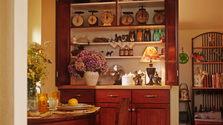 A classy, wooden kitchen hutch filled with a variety of items, lit by warm lighting