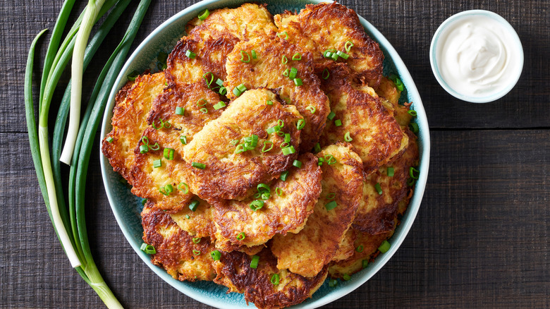 latkes with scallions in a plate with a bowl of sour cream on the side