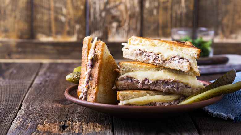 Four tuna melt halves stacked on a plate with pickle spears