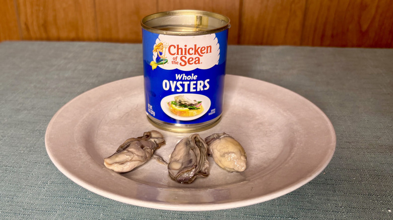 A can of Chicken of the Sea Whole Oysters behind three individual oysters on a plate