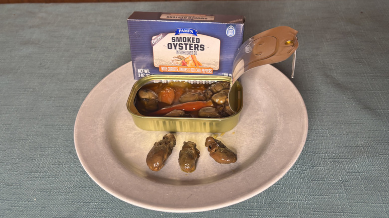A box and can of Pampa Smoked Oysters sitting behind three individual oysters on a plate