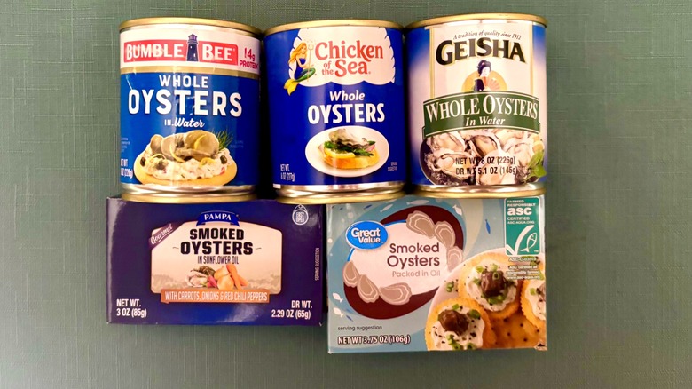 Five containers of canned oysters laid out - top left to right: Bumble Bee Whole Oysters in Water, Chicken of the Sea Whole Oysters, and Geisha Whole Oysters in Water - Bottom left to right: Pampa Smoked Oysters in Sunflower Oil with Carrots, Onions and Red Chili Peppers, and Great Value Smoked Oysters Packed in Oil