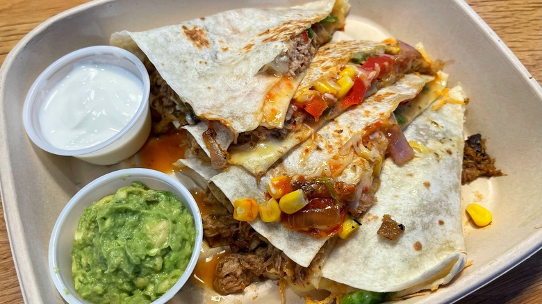 A corn-and-veggie-stuffed quesadilla with sides of sour cream and guacamole