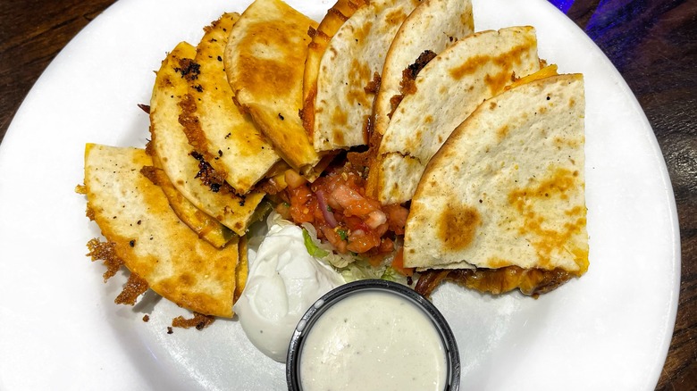 A crispy quesadilla on a round plate with ranch and sour cream