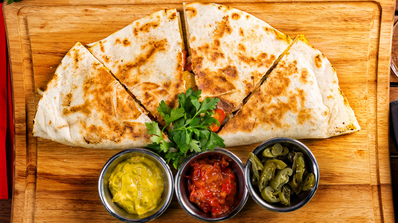 A quesadilla cut into four pieces on a wooden cutting board