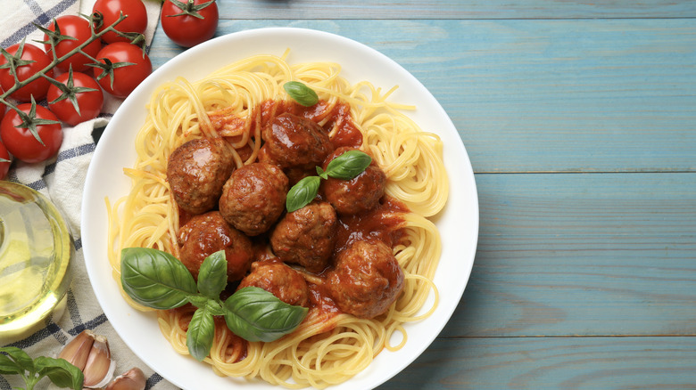 A plate of spaghetti and meatballs topped with fresh basil next to fresh cherry tomatoes on the vine