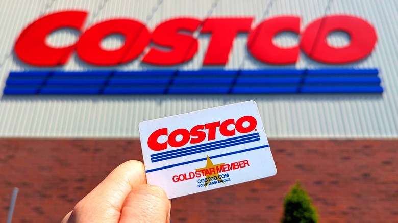 Hand holding a Costco Gold Star membership card in front of a Costco storefront