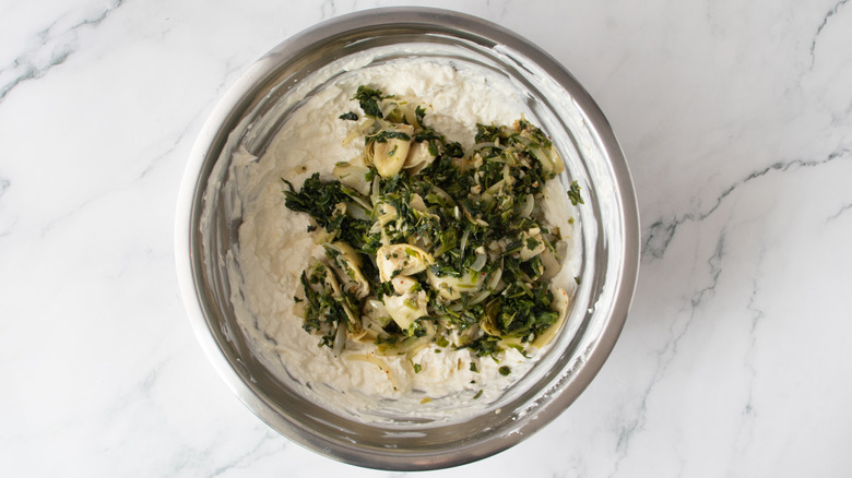 cooked spinach on top of white creamy substance in a metal bowl